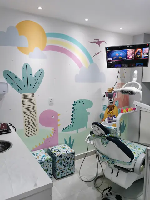Cadeira do consultório diante da parede pintada, com a TV acesa no alto.