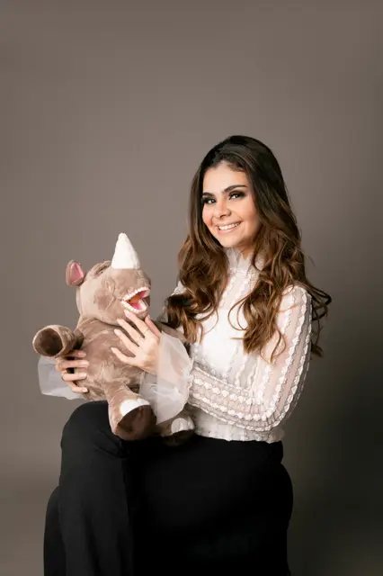 A Dra. Desirée hoje, sorrindo, segurando uma pelúcia com dentes usada nas consultas.