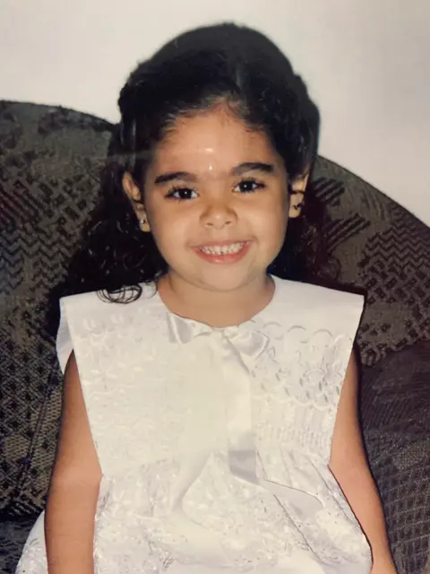 Desirée criança, sorrindo, de vestido branco.